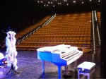 Imagen de piano de cola blanco en escenario de teatro con butacas de fondo